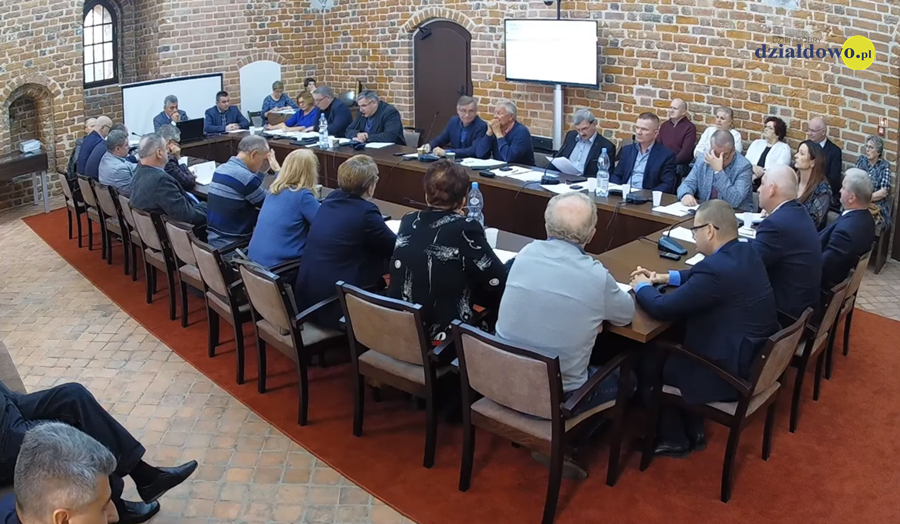 Na zdjęciu widać radnych i osoby uczestniczące w sesji rady miasta, sesja odbywa się w sali zamkowej uczestnicy siedzą za stołem