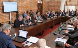 (Na zdjęciu widać radnych i osoby uczestniczące w sesji rady miasta, sesja odbywa się w sali zamkowej uczestnicy siedzą za stołem)
