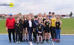 grupa osób, zawodnicy UKS MOSiR Działowo stoją na bieżni stadionu z gościem honorowym mityngu Lidią Chojecką