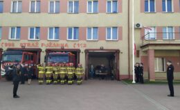 stoją strażacy przed budynkiem Komendy. Na maszt wciągana jest flaga polski
