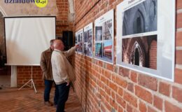 dwie osoby oglądają wystawę w zamkowej kaplicy, plansze ze zdjęciami i opisem