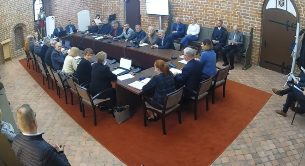 widać radnych i osoby uczestniczące w sesji rady miasta, sesja odbywa się w sali zamkowej, uczestnicy siedzą za stołem