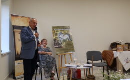 kobieta siedzi (artystka), a mężczyzna przemawia do mikrofonu (wójt)