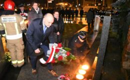 grupa osób składa kwiaty przy tablicy pamiątkowej