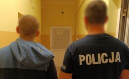 policjant i osoba zatrzymana stoją tyłem do obiektywu w korytarzu