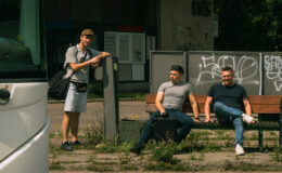 widać trzech mężczyzn, jeden stoi dwóch siedzi na ławce
