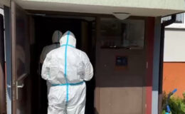widać dwie osoby w kombinezonach wchodzące do klatki schodowej w bloku