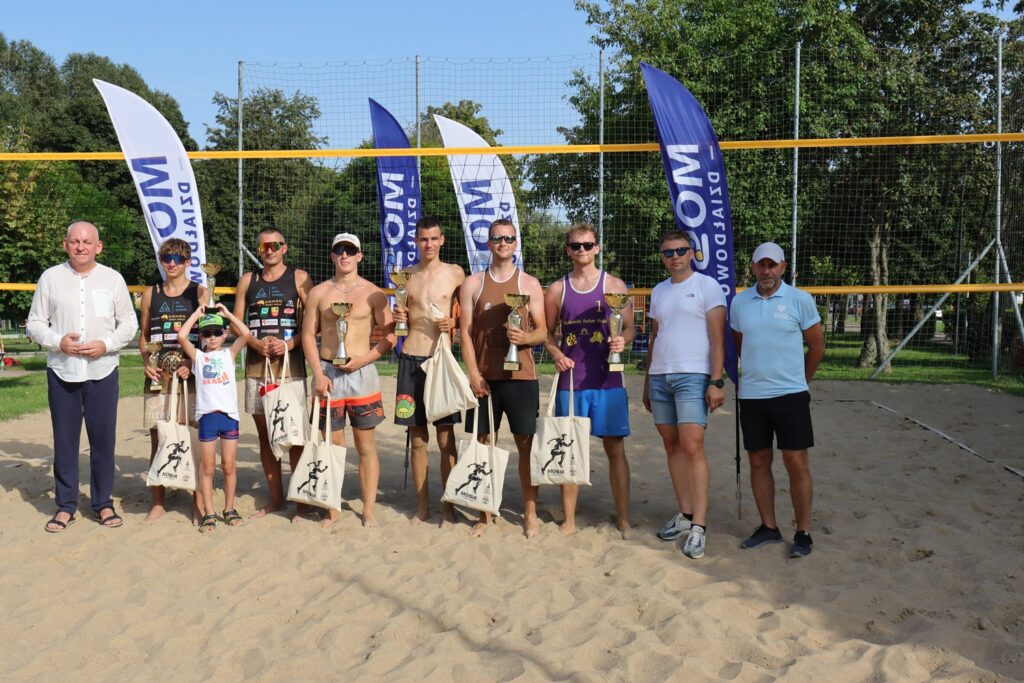 Siatkówka plażowa na Urodziny Działdowa stoi grupa mężczyzn, uczestnicy turnieju z burmistrzem, dyrektorem MOSiR i sędzią