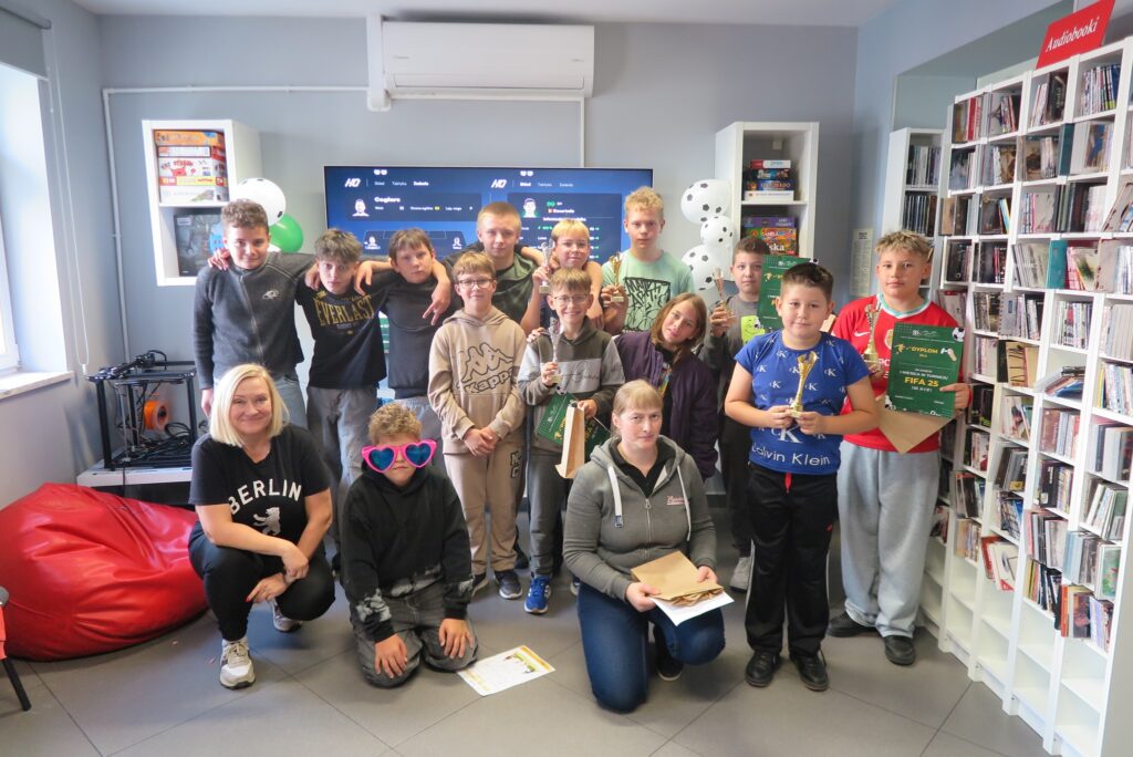 Turniej FIFA 2025 w bibliotece - znamy zwycięzców pamiątkowa fotografia uczestników Turnieju wraz z panią dyrektor i panią bibliotekarką