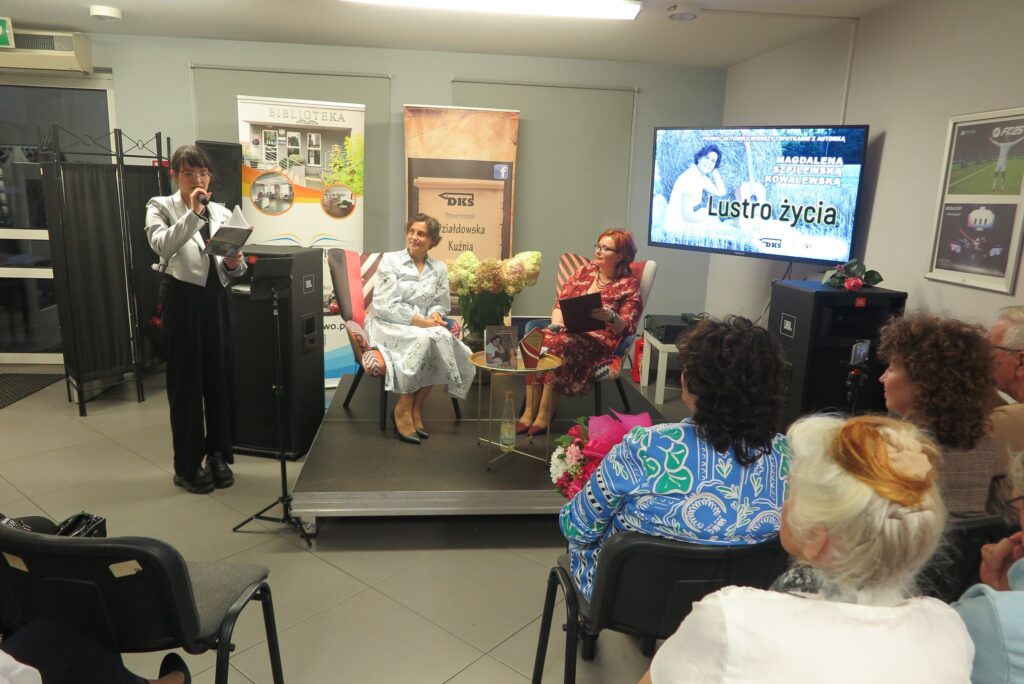 jedna osoba czyta przy mikrofonie, a dwie osoby siedzą