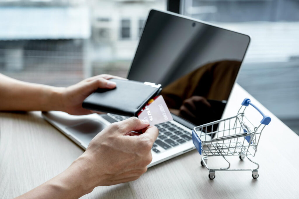 Mężczyzna stracił ponad 8000 zł. Bez telewizora i bez pieniędzy - kolejny oszukany w Internecie komputer dłonie, portfel, kartę płatniczą mały koszyk na zakupy / ilustracja do treści