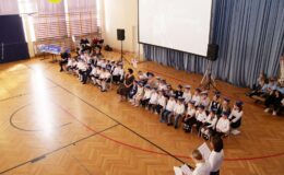 siedzi grupa dzieci i nauczycieli, w sali gimnastycznej Szkoły Podstawowej nr  4  w Działdowie