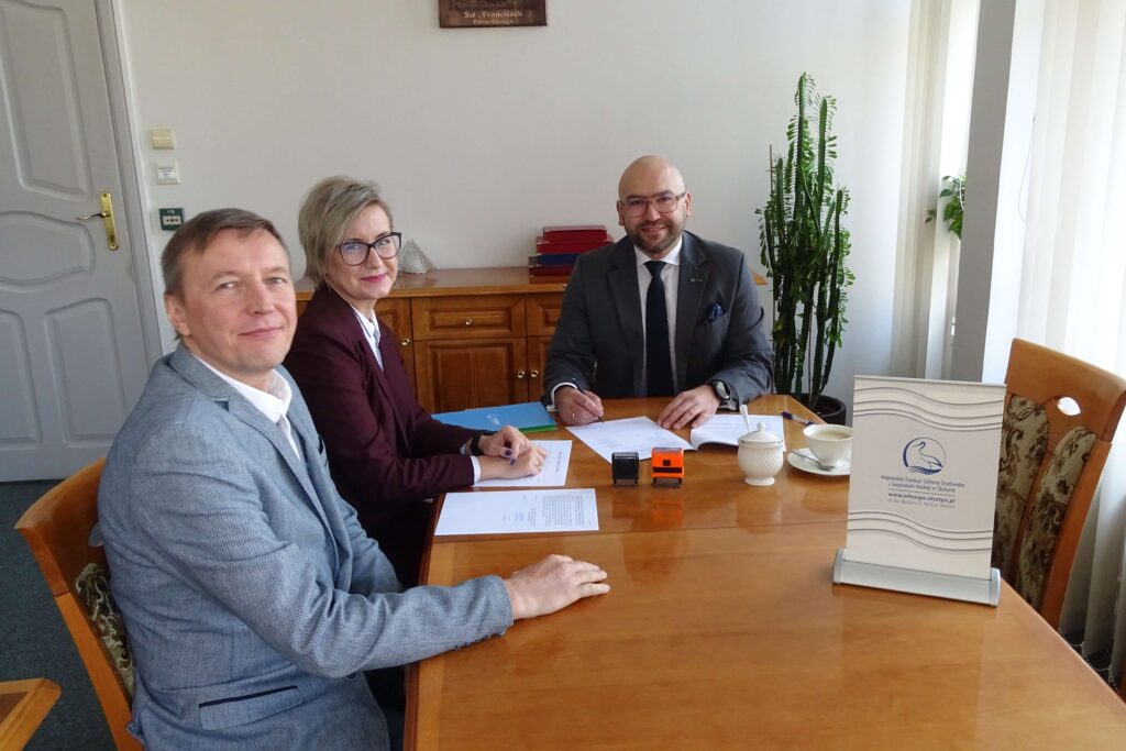 widać trzy osoby siedzące przy stole, jedna kobieta i dwóch mężczyzn