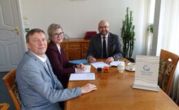 widać trzy osoby siedzące przy stole, jedna kobieta i dwóch mężczyzn
