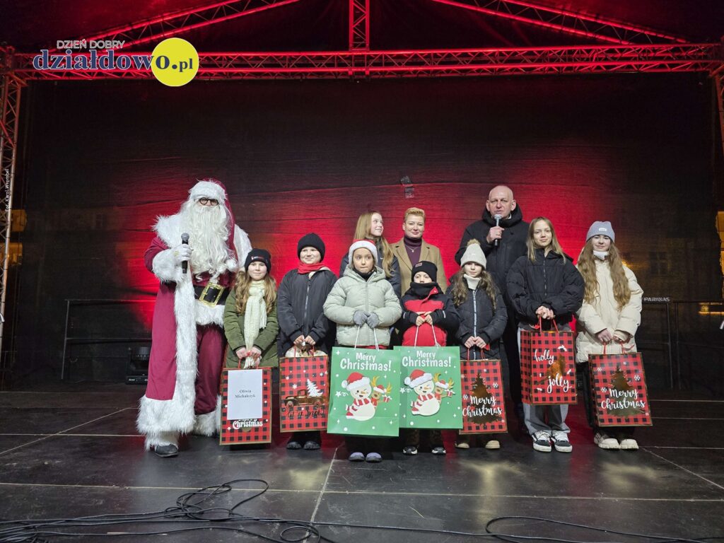 burmistrz, osoby dorosłe, dzieci i młodzież stoją na scenie, podczas ogłoszenia wyników konkursu na "Świąteczną Kartkę Bożonarodzeniową"