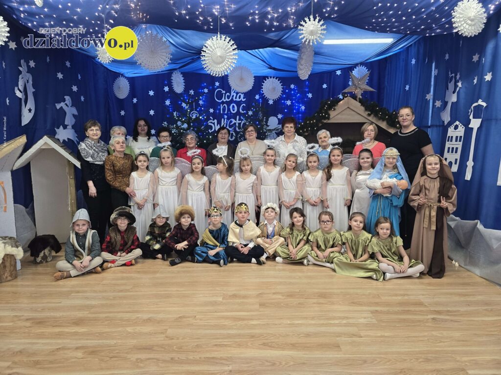 Na zdjęciu głównym występujące dzieci wraz z paniami, dzieci stoją i siedzą, panie stoją, pamiątkowa fotografia