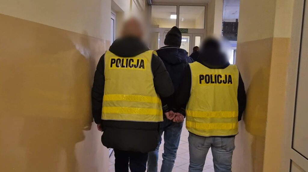 prowadzenie zatrzymanego w kajdankach przez funkcjonariuszy w kamizelkach policyjnych / fot. policja