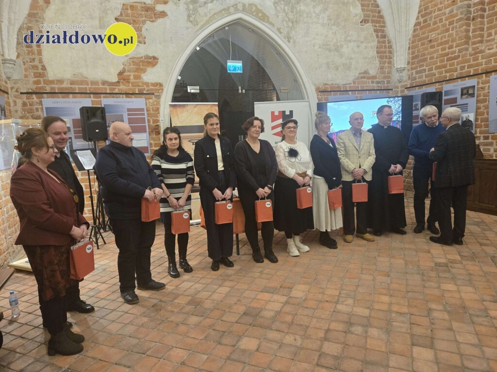 pamiątkowa fotografia autorów zaangażowanych w publikację "Obóz Soldau - by człowiek pamiętał", widać kobiety i mężczyzn stojących w sali zamkowej,