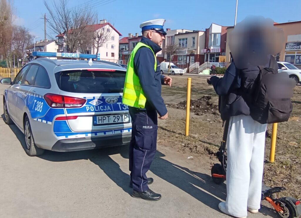 policjant, policyjny radiowóz i osoba stojąca z hulajnogą / fot. policja