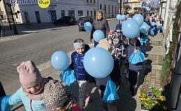 chodnikiem idzie grupa przedszkolaków, trzymająca niebieskie baloniki