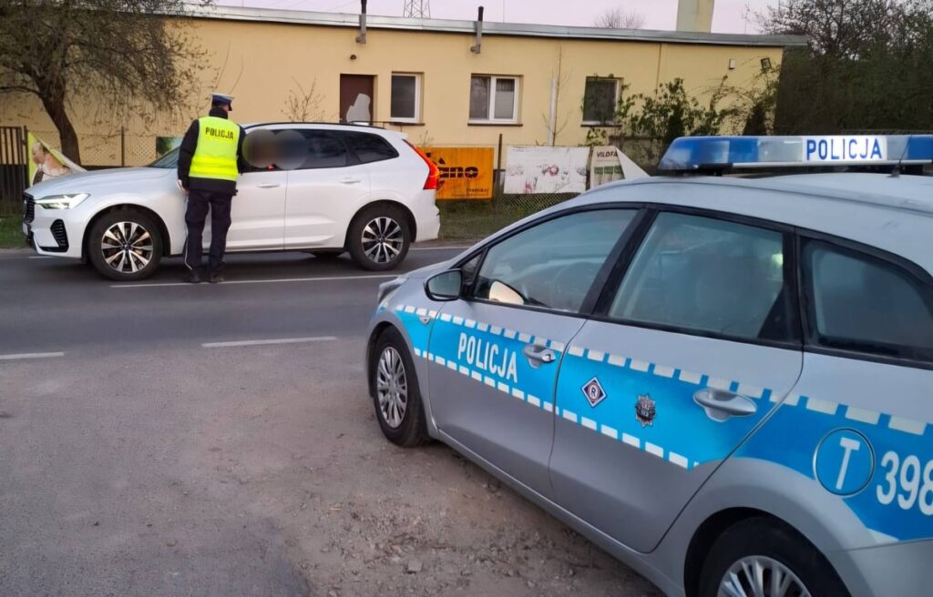 policjant badający trzeźwość kierowcy, na zdjęciu widać radiowóz i samochód osobowy / fot. policja