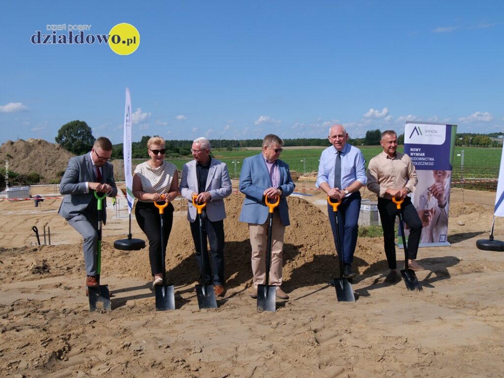 grupa osób stojąca na miejscu inwestycji, gdzie powstanie blok w ramach Społecznej Inicjatywy Mieszkaniowej KZN Warmia i Mazury