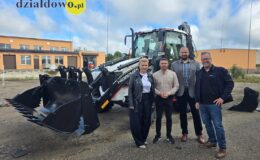 kobieta i trzech mężczyzn na tle koparko-ładowarki