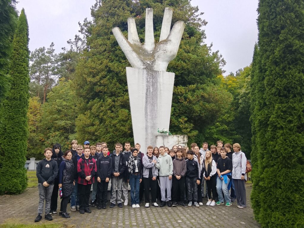 grupa uczniów i panie nauczycielki ze Szkoły Podstawowej im. Arcybiskupa Antoniego Juliana Nowowiejskiego w Słupnie na cmentarzu i przy pomniku w Lesie Komornickim